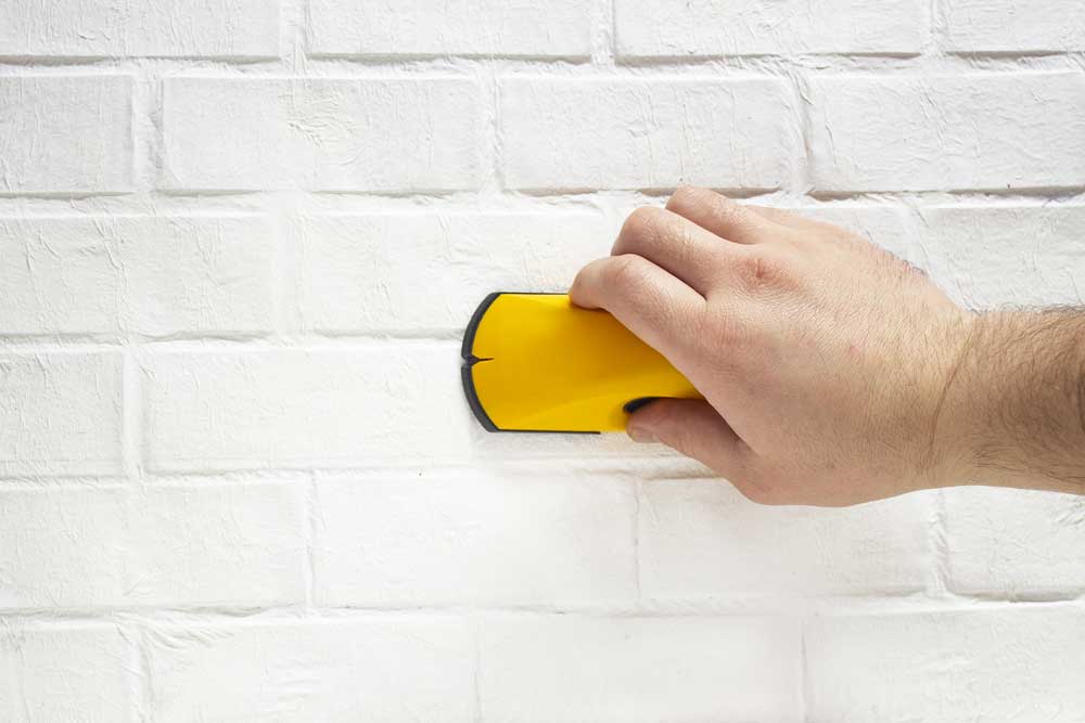 A man works with a wireless building tool to detect wooden battens.