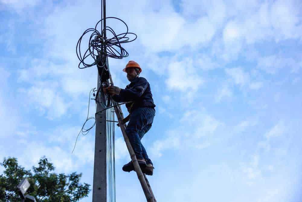 A worker is working from a utility pole ladder.